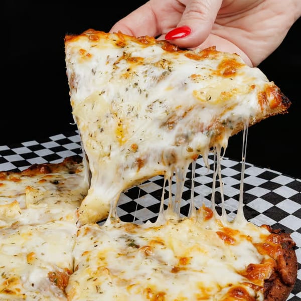 A hand with red nail polish lifts a slice of cheesy pizza, stretching the melted cheese.