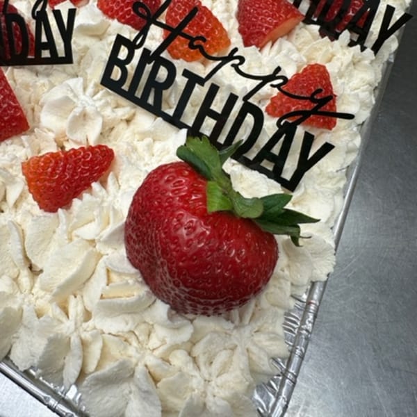 A birthday cake with whipped cream, strawberries, and "Happy Birthday" toppers.