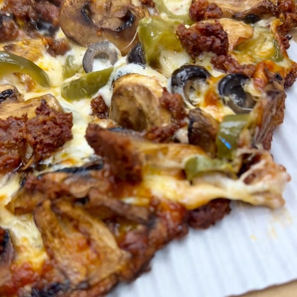 Close-up of a pizza slice with melted cheese, mushrooms, green peppers, black olives, and sausage.