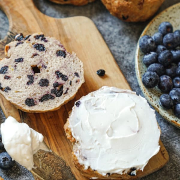Blueberry bagel, sliced and spread with cream cheese, next to a bowl of fresh blueberries.