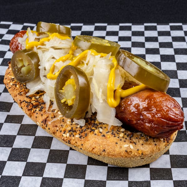Gourmet hot dog with sauerkraut, sliced jalapeños, and mustard on a seeded bun.