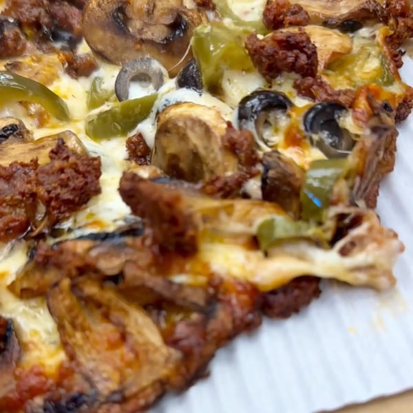 Close-up of a pizza slice with melted cheese, green peppers, black olives, and sausage.